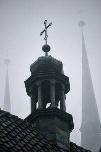 Wieżyczka starego kościoła z krzyżem na tle gęstej mgły, z dwoma dalszymi wieżami ledwo widocznymi w oddali – melancholijne zdjęcie uchwycone przez fotograf architektury, które skupia się na sylwetkach sakralnych elementów w niepogodzie. Wrocław