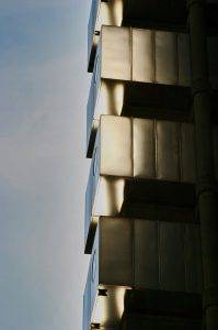 Zbliżenie nowoczesnej fasady budynku z metalowymi segmentami, sfotografowane przez fotografa architektury, z dramatycznym światłocieniem podkreślającym geometryczną strukturę. Loyds Building London UK