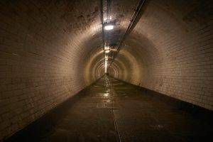 Fotograf architektury ukazał długi, wąski tunel wyłożony jasnymi cegłami, z wilgotną podłogą i oświetleniem biegnącym przez środek sufitu, tworzącym wrażenie nieskończonej perspektywy. London UK